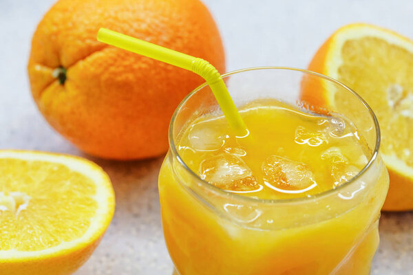A few oranges and a glass of fresh orange juice with ice on a light gray background