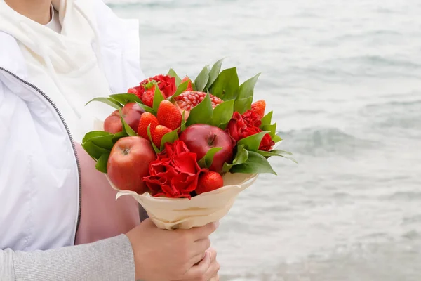 Bouquet of flowers and fruits in the hands of a woman on a background of the sea