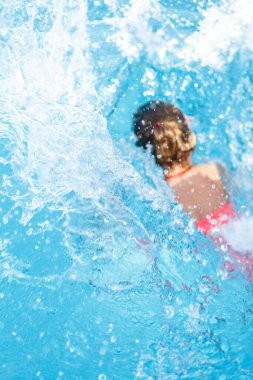 Küçük kız havuza düşer, spreyine odaklanır.