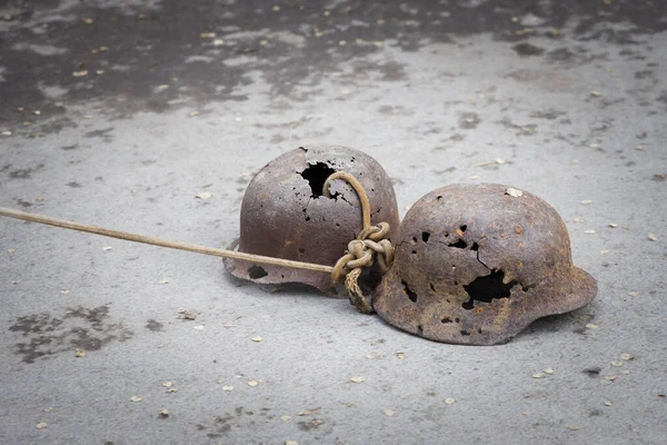 Two german military helmets perforated with bullets pull on a rope on asphalt as a symbol of victory over the Nazi invaders