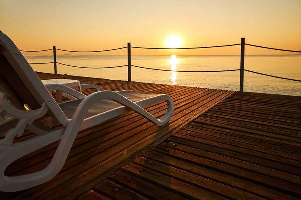 穏やかな海と昇る太陽を背景に ビーチラウンジャーは木製の桟橋に立っています — ストック写真