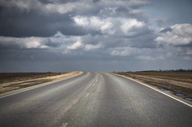 Gök gürültüsü bulutlarına doğru uzanan asfalt yolu olan doğal manzara.