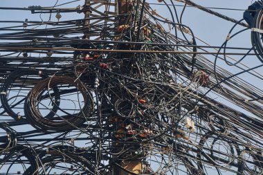 Mavi gökyüzüne karşı birbirine dolanmış bir sürü elektrik kablosu.