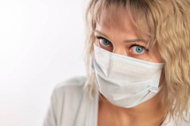 Beyaz arka planda maske takan mavi gözlü, beyaz saçlı, çekici, beyaz tenli sarışın kadın.