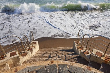 Taş adımlar kumlu bir plaja doğru iniyor.