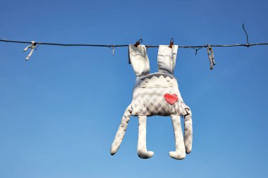 Unutulmuş eski bir tavşan oyuncağı. Arka plandaki çamaşır ipinde asılı. Mavi gökyüzünde.