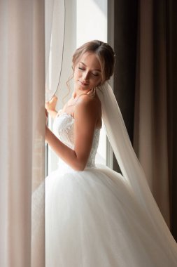 Gelinlik giymiş hoş bir kız pencerede duruyor.