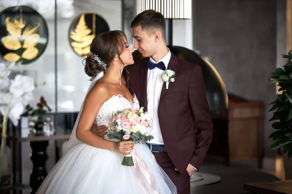 Beyaz elbiseli güzel bir gelin ve bordo takım elbiseli yakışıklı bir damat birbirine bakıyor.