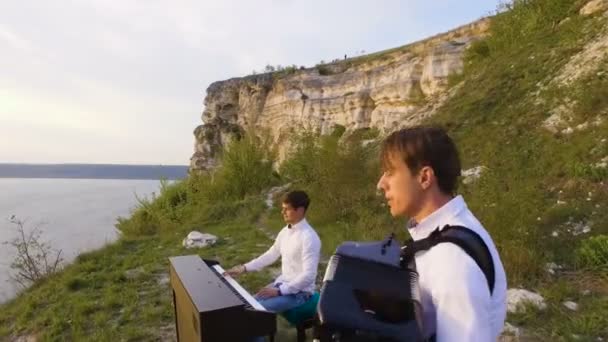 Dois músicos Pianista e acordeonista tocando nas rochas ao pôr do sol sobre o mar — Vídeo de Stock