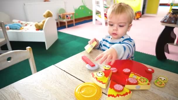 Μικρό αγόρι παίζει με πολλά πολύχρωμα πλαστικά μπλοκ, μπάλες, κουζίνα στο δωμάτιο — Αρχείο Βίντεο