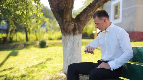 Een jonge man zittend op een groen bankje in het park en wachten op een vergadering — Stockvideo