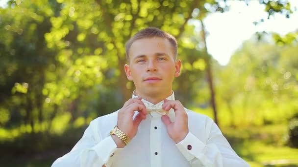 Hombre el novio en camisa blanca para corregir pajarita al aire libre. Luz natural — Vídeos de Stock