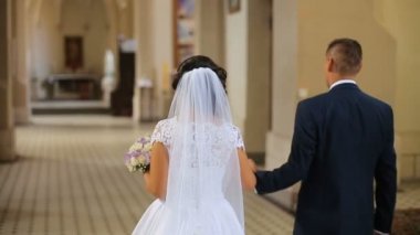 Zarif gelin ve damadın eski kilisede yürürken el ele tutuşarak Mavi takım elbise
