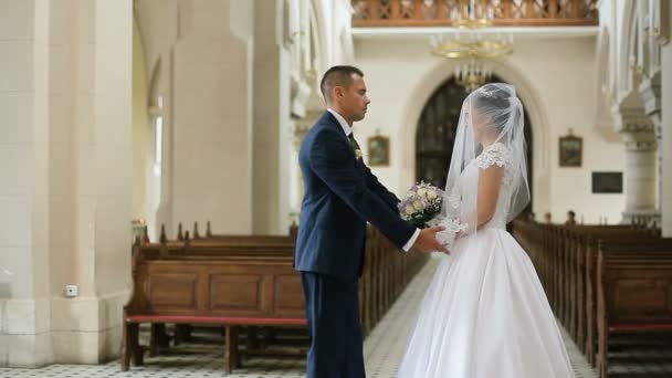 Элегантные невеста и жених в синем костюме, держась за руки, прогуливаясь по старой церкви — стоковое видео