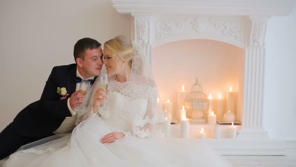 Bride and groom pose to the photographer in studio near fireplace with champagne — Stock Video
