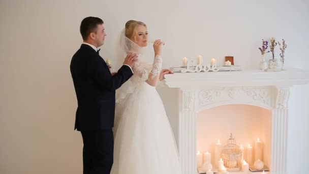 Bruid en bruidegom poseren voor de fotograaf in de studio in de buurt van open haard met champagne — Stockvideo