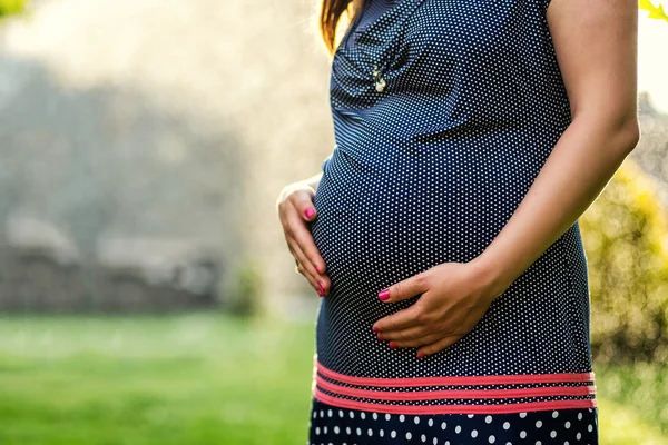 Foto da barriga da mulher grávida. Mãos a abraçar a barriga grávida. Close up de mãos humanas segurando barriga grávida. A mulher grávida abraça a barriga. Gravidez. Conceito de gravidez — Fotografia de Stock