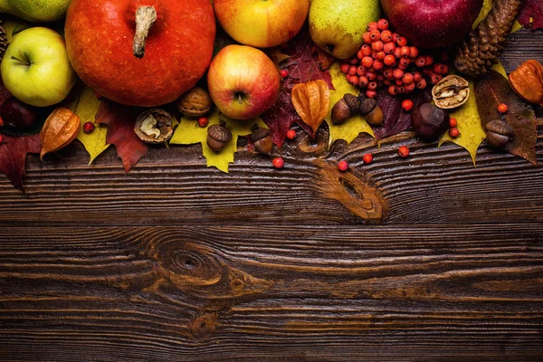 autumn still life, harvested pumpkins with fall leaves and autumn fruit, gifts of autumn, copy space, wooden background, walnuts, maple leaves - autumn composition from top. Free space for text