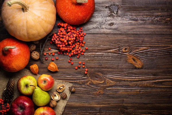 autumn still life, harvested pumpkins and autumn fruit, gifts of autumn, copy space, wooden background, walnuts, maple leaves - autumn composition from top. Free space for text