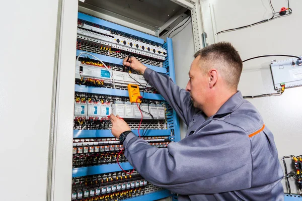 electrician testing industrial machine, electrician builder engineer screwing equipment in fuse box, Male Electrician