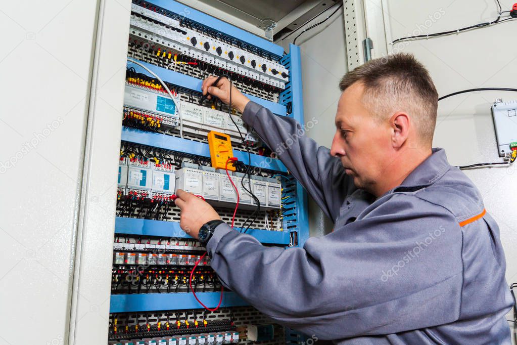 electrician testing industrial machine, electrician builder engineer screwing equipment in fuse box, Male Electrician