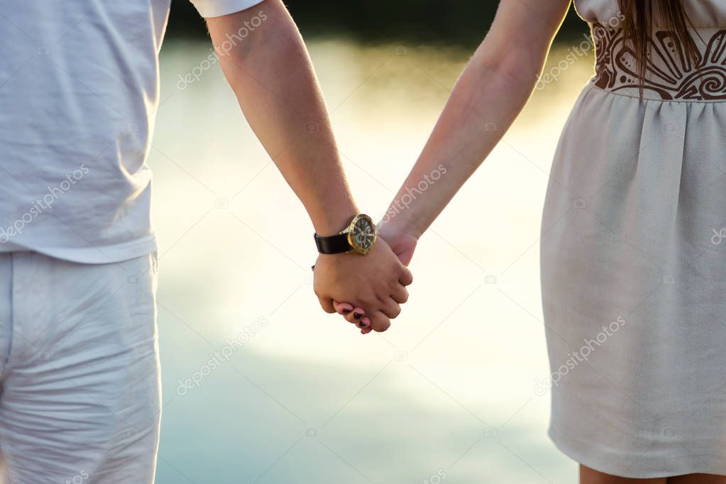 young couple holding hands on the shore of the river, hands close-up, love, feelings, sunset on the river, bouquet of daisies