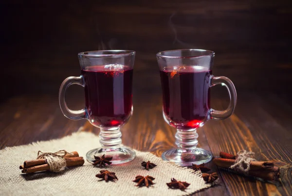 Dos copas, taza de vino caliente rojo drink.Mulled sobre fondo de madera con especias de Navidad, rebanada de naranja, palitos de anís y canela, close up. — Foto de Stock