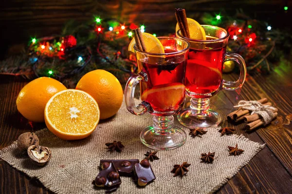 Два стакана, чашка красного горячего напитка.Вино на деревянном фоне с рождественскими специями, оранжевый ломтик, закрыть .Christmas глинтвейно.Ветвь елки, рождественские огни — стоковое фото