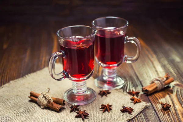 Dos copas, taza de vino caliente rojo drink.Mulled sobre fondo de madera con especias de Navidad, rebanada de naranja, palitos de anís y canela, close up. — Foto de Stock