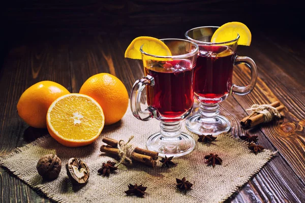 Dos copas, taza de vino caliente rojo drink.Mulled sobre fondo de madera con especias de Navidad, rebanada de naranja, palitos de anís y canela, close up. — Foto de Stock