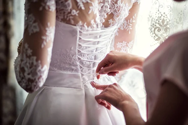 La mañana de la novia, la novia lleva el vestido, la dama de honor corrige el arco en el vestido, la boda, el vestido hermoso —  Fotos de Stock