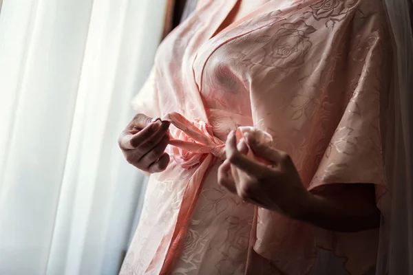 Chica en una bata rosa en la ventana, la mañana de la novia, la chica ata el cinturón en la bata — Foto de Stock