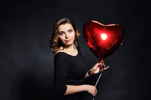Piękna dziewczyna trzyma duży czerwony balon w formie serca, Walentego Day.Red serca Zamknij się, piękno portret twarz kobiety z makijaż, sexy błyszczący makijaż usta i ciemne brwi, koncepcję makijażu — Zdjęcie stockowe