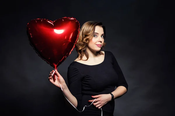 Mooi meisje met een grote rode ballon in de vorm van harten, Valentijnsdag Day.Red hart dicht omhoog, portret van de schoonheid van de vrouwelijke gezicht met make-up, sexy gloss lippen make-up en donkere wenkbrauwen, make-up concept — Stockfoto