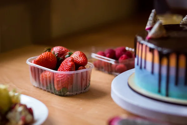 chocolate cake with multicolored shortcakes decorated by dragon fruit with Organic fresh kiwi fruit and half of dragon fruit  on a wooden cutting board,red ripe strawberry in plastic box