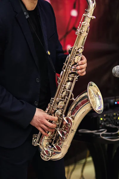 Saxofón dorado con manchas en las manos masculinas en el fondo rojo.Manos del músico tocando saxofón alto, primer plano, Manos del novio tocando el saxofón, concepto de música de jazz — Foto de Stock