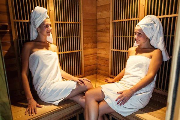 享受令人心旷神怡的两个女孩呆在桑拿浴室，两个快乐的女人在桑拿、 桑拿概念、 水疗概念互相交谈，放松在木制水疗房 — 图库照片