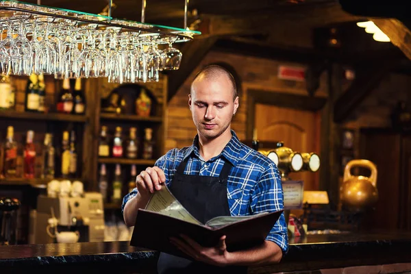 Barman at work in pub,Portrait of cheerful barman worker standing,Waiter giving menus,A pub.Bar.Restaurant.Classic.Evening.European restaurant.European bar.American restaurant.American bar.