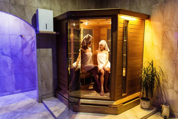 Twee meisjes genieten van een ontspannen verblijf in de sauna, twee gelukkige vrouwen in een sauna, sauna concept, spa concept met elkaar praten, ontspannen in houten spa Kamerinformatie — Stockfoto