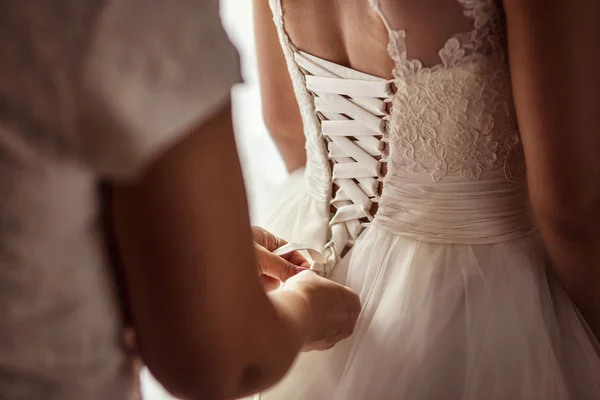 La mañana de la novia, la novia lleva el vestido, la dama de honor corrige el arco en el vestido, la boda, el vestido hermoso —  Fotos de Stock