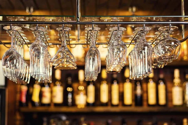Glasses hanging over a bar rack,Cocktail glasses hanging over a bar,different glasses hanging over the bar. Soft focus,Clean washed and polished glasses,A pub.Bar.Restaurant. — Stock Photo, Image