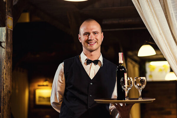 Официант предлагает посетителям вино, официант в форме ждет заказа, официант с белым полотенцем на руке, уверенный официант, лоб. Ресторан.Классиция.Вечером. Европейский ресторан
