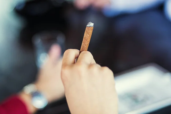 man\'s hand with a cigar on a glass of whiskey background,Person holding a cigar,man burning up a cigar - close up