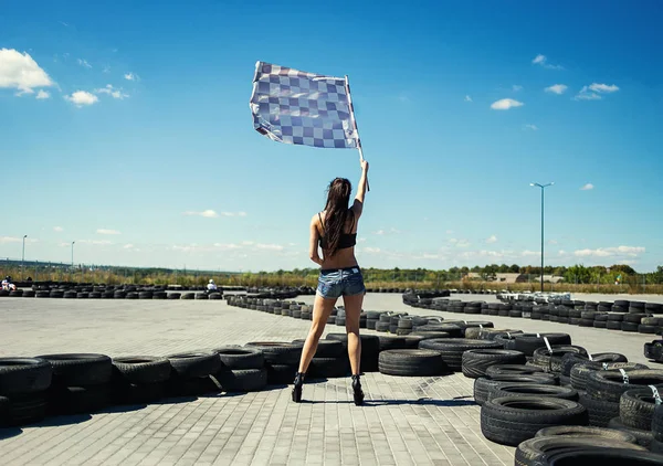 Sexy junge Frau mit Rennflagge. Kartschiedsrichter mit Fahne auf Go-Kart-Start gegen Rauch, Go-Kart-Rennfahrer draußen bei blauem Himmel — Stockfoto