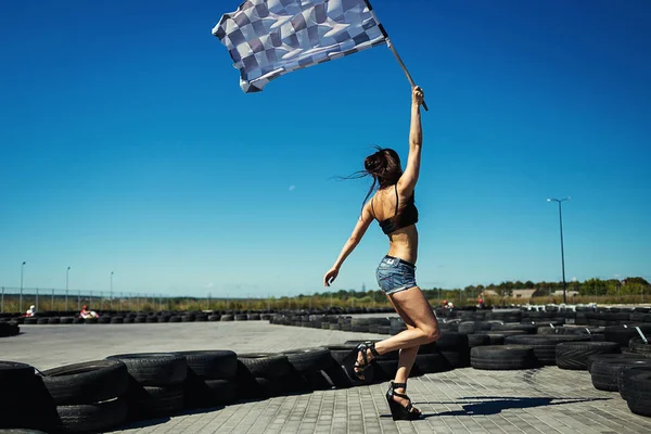 Sexy junge Frau mit Rennflagge. Kartschiedsrichter mit Fahne auf Go-Kart-Start gegen Rauch, Go-Kart-Rennfahrer draußen bei blauem Himmel — Stockfoto