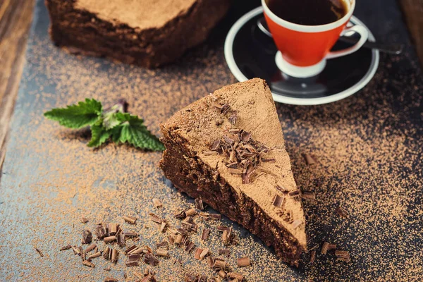 Pastel de chocolate con caramelos y taza de café, pastel de chocolate con una pieza cortada y hoja sobre fondo gris, primer plano, pastel de chocolate negro, pastel de chocolate vegano, pastel de chocolate sabroso sobre fondo de madera — Foto de Stock