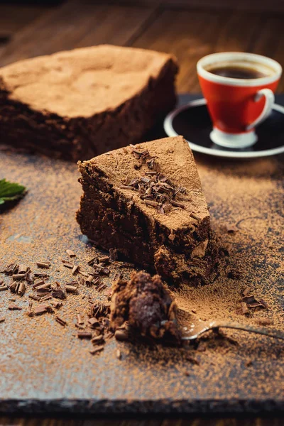 Шоколадный торт с конфетками и чашкой кофе, шоколадный торт с нарезанным кусочком и лезвием на сером фоне, крупный план, темный шоколадный торт, веганский шоколадный торт, вкусный шоколадный торт на деревянном фоне — стоковое фото