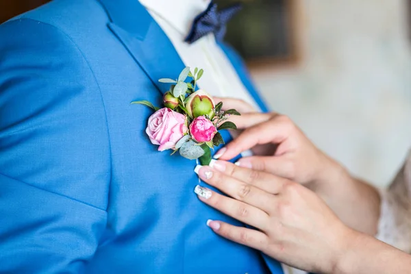 Girl corrects bride groom boutonniere. flowers Advertising.Wedding. Bride corrects groom boutonniere at their wedding. Close-up details.hang of a bride adjusting boutonniere on grooms jacket.