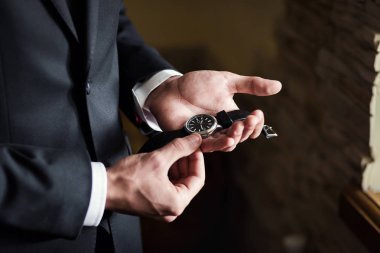 İş adamı kol saatini kontrol ediyor, saati eline alıyor, damat düğün töreninden önce hazırlanıyor.