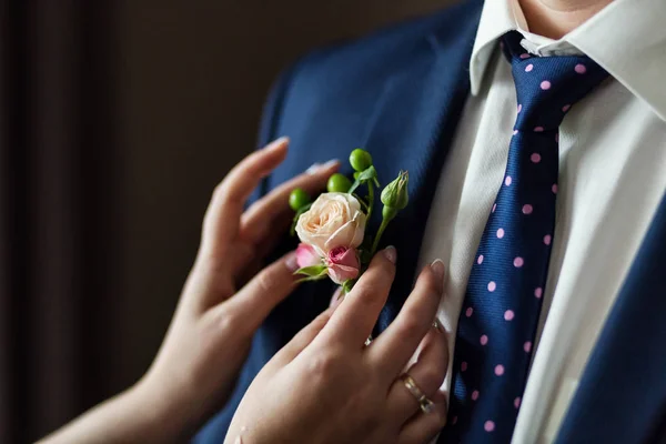 Bride corrects groom boutonniere on jacket at their wedding close-up details — Stock Photo, Image